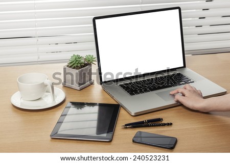 A working wooden desk(table) with notebook computer, tablet pc, mobile, hand phone, coffee cup, globe, pencil, behind white blind(roller blind) and hand.
