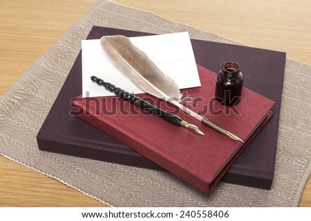 envelope, letter, ink, feather quill pen, red book, diary, sketch book on the wooden office desk(table) behind white blind.