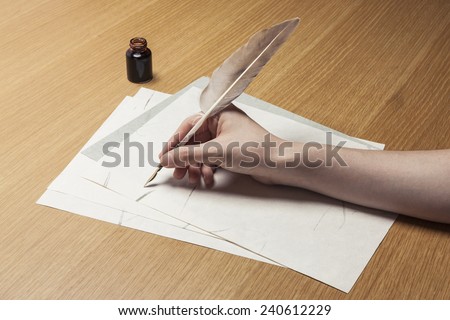 A female(woman) hand hold(write) a feather quill pen with ink on the letter paper and wood desk(table) at the studio.