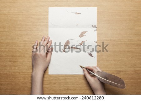A female(woman) hand hold(write) a feather quill pen on the letter paper and wood desk(table) top view at the studio.