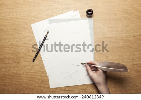A female(woman) hand hold(write) a feather quill pen with ink on the letter paper and wood desk(table) top view at the studio.