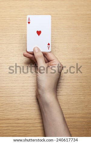 A female(woman) hand hold a trump card(heart, a) on the wood office desk(table) top view at the studio.