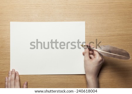 A female(woman) hand hold a feather quill pen with letter paper on the wood office desk(table) top view at the studio.