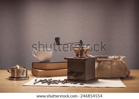 A coffee grinder and book, cup, dripper, linen bag on the wood table(desk).