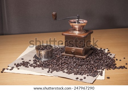 A brass coffee dripper, grinder, beans, table cloth on the wood table(desk).
