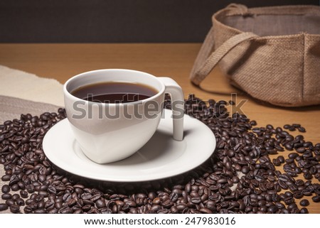 A white coffee cup, saucer and coffee beans on the table cloth and wood table(desk).