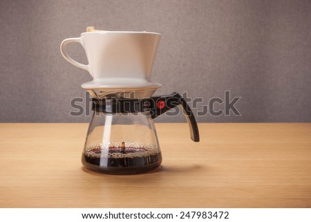 A white ceramic coffee cup(dripper) and glass pot for hand drip coffee on the wood table(desk).