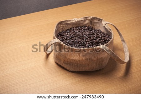 Many coffee beans in the linen bag on the wood table(desk).