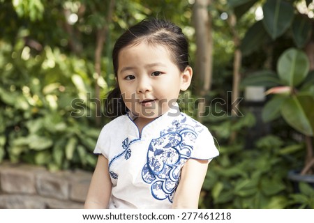 A girl(kid) wearing Chinese traditional clothes(dress, chipao) with big smile in the botanical garden at the spring,