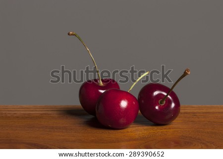 Three fresh red cherry in the white ceramic bowl(container) on the wood table(desk) in the grey background at the studio.