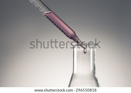 A man\'s hand hold and lean a glass dropping pipet(dropping pipette, medicine dropper, spuit) with red(magenta, pink) water(liquid, fluid) to the glass Erlenmeyer flask in the laboratory