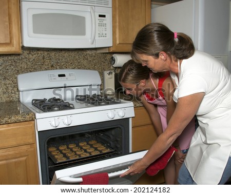 Mother and daughter baking cookies together, taking cookies out of the oven