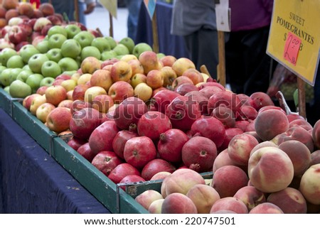 fruit stand at a local farmers market with green apples, red apples, pomegranates and peaches displayed for sale