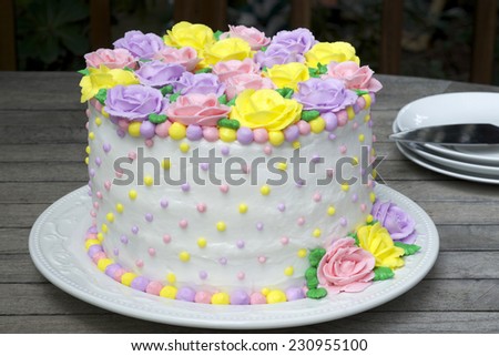 Pastel Rainbow Yellow, Pink, Purple butter cream frosting handmade roses on a round cake frosted with white icing and embellished with yellow, pink and purple dots of buttercream frosting.