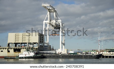 OAKLAND, CA - DECEMBER 29, 2014: FOSS Tugboat POINT VINCENT moving a Cargo Barge ship through the Inner Harbor at the Port of Oakland. It will dock with Matson Cargo Ship MANOA to provide services.