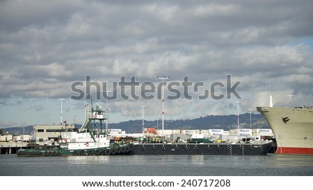 OAKLAND, CA - DECEMBER 29, 2014: FOSS Tugboat POINT VINCENT moving a Cargo Barge ship through the Inner Harbor at the Port of Oakland. It will dock with Matson Cargo Ship MANOA to provide services.