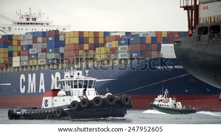 OAKLAND, CA - JANUARY 27, 2015: Tugs move vessels that should not move themselves, such as ships in a crowded harbor. Tugboat VETERAN at the Stern of a Cargo Ship as it enters the Port of Oakland.