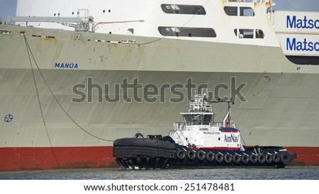 OAKLAND, CA - FEBRUARY 09, 2015: AmNav Tugboat REVOLUTION on the Port side of Matson Cargo Ship MANOA as it enters the Port of Oakland. A tugboat maneuvers vessels by pushing or towing them.