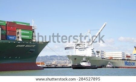 OAKLAND, CA - JUNE 01, 2015: Tugboat REVOLUTION at the bow of Cargo Ship EVER SALUTE, assisting the vessel to depart the Port of Oakland as Tugboats push Matson Cargo Ship MANOA arriving at the port.