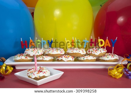 Miniature donut cake on long white plate with happy birthday candles one donut on single square plate with single pink candle. Perfect first birthday party idea for small hands toddler and children
