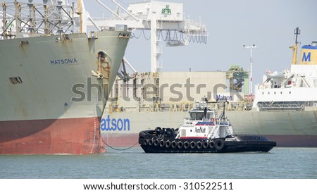 OAKLAND, CA - AUGUST 17, 2015: A tugboat maneuvers vessels by pushing or towing them. Tugboat REVOLUTION at the bow of Cargo Ship MATSONIA, assisting the vessel to maneuver into the Port of Oakland.