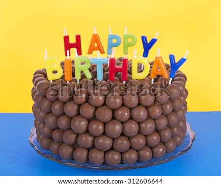 Whopper of a Chocolate Birthday Cake decorated with candy malt balls and Happy Birthday Candles. Blue surface yellow background. Fast and easy home made cake for children or adult birthday party