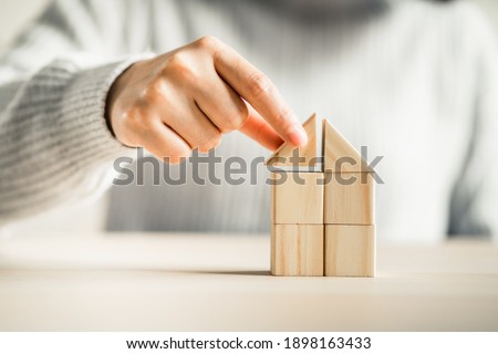 women putting triangle wooden block for show the construction of a wooden in the shape of a house,
Build a home concept.