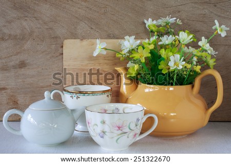 Flower in a yellow tea pot and vintage cup of coffee on wooden background, cozy home rustic decor, cottage living