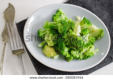 Freshly steamed broccoli served with small plate with fork and napkin on white table