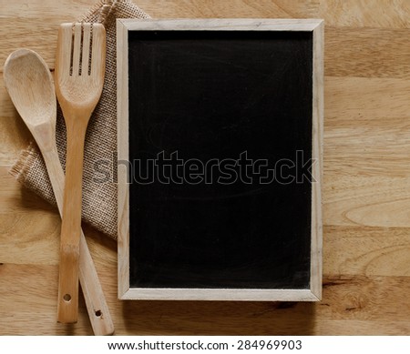 Blackboard on wooden surface and serving spoons with napkin, cooking concept