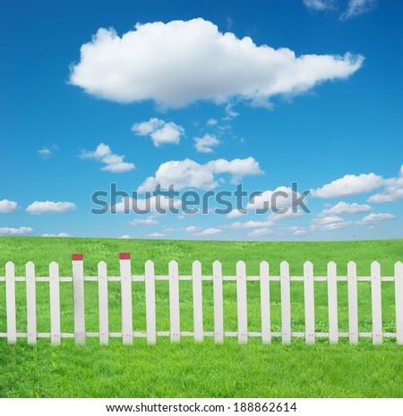 The white fence and green grass under blue sky and white clouds.