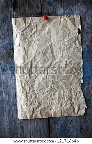 Old yellowed sheet of crumpled paper, attached to the weathered wooden surface of the red pin