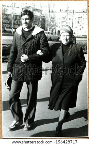LUGANSK - CIRCA 1990: middle-aged woman walking down the street arm in arm with a young man, Lugansk, Ukraine, 1990