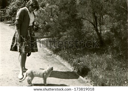 GERMANY, ROSTOCK - 1950s: An antique photo shows woman with cat on the footpath in the park
