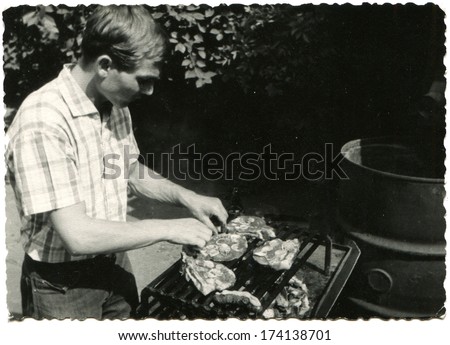 GERMANY -  1950s: An antique photo shows man grilling sausages on the grill
