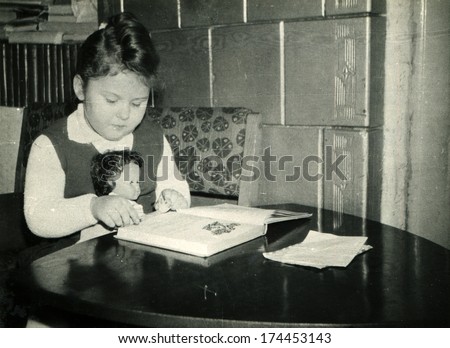 GERMANY -  CIRCA 1965: An antique photo shows girl with puppy read book at the table
