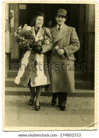 GERMANY -  CIRCA 1930s: An antique photo shows woman in a fur coat with a bouquet of flowers walking arm in arm with a man in a coat and hat