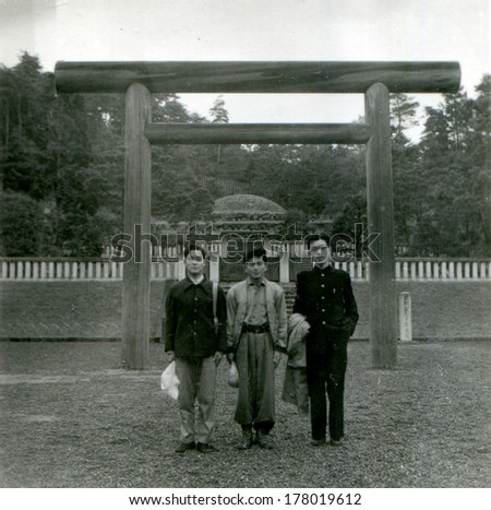 JAPAN  - 1950s: An antique photo shows three young men on the background of the temple gate. Sacred gate, Torii (\
