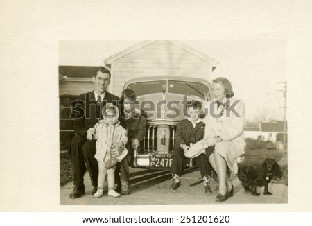 TEXAS, USA - CIRCA 1940s: Reproduction of an antique photo shows American family with three children, two boys and a girl posing sitting on the bumper chic De Soto Series S-8 Custom Coupe, 1941