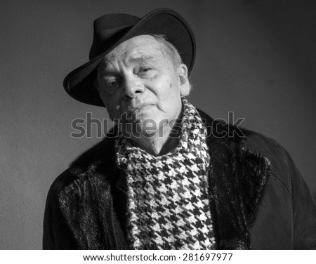 Portrait of elderly man in coat, hat and scarf on a dark background