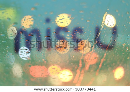 Rain drops and miss you text on window with light bokeh, rainy season abstract background.