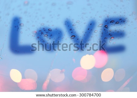 Rain drops with the word love write on window with light bokeh, rainy season abstract background.
