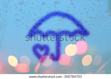 Rain drops and umbrella and heart write on window with light bokeh, rainy season abstract background.