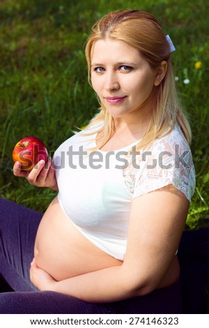 Portrait of pregnant woman outdoors, new life concept, relaxing in park with apple