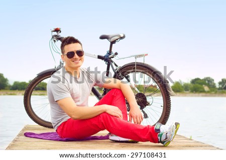 young man sitting at the beach and resting after bicycle ride