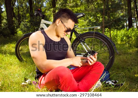 young man sitting in the park  with phone and resting after bicycle ride