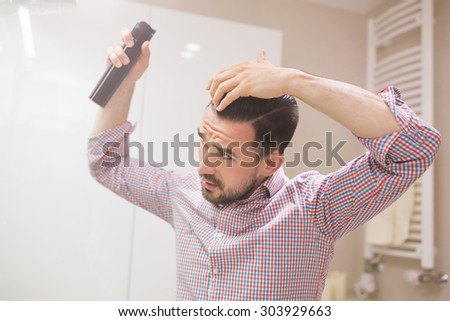 Latin beardy man using hair spray to strengthen his hair style