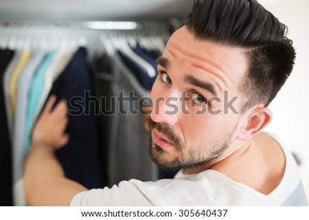 Serious man looking at camera when selecting a jacket from a row in shop.