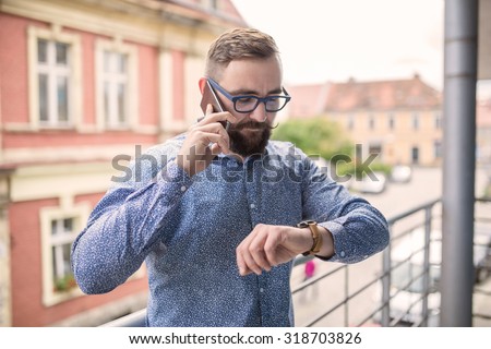 Man standing at balcony, looking at hand watch and calling