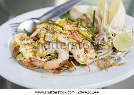 Seafood pad Thai dish of Thai fried rice noodles on a square white plate with chopsticks and grated carrot garnish.